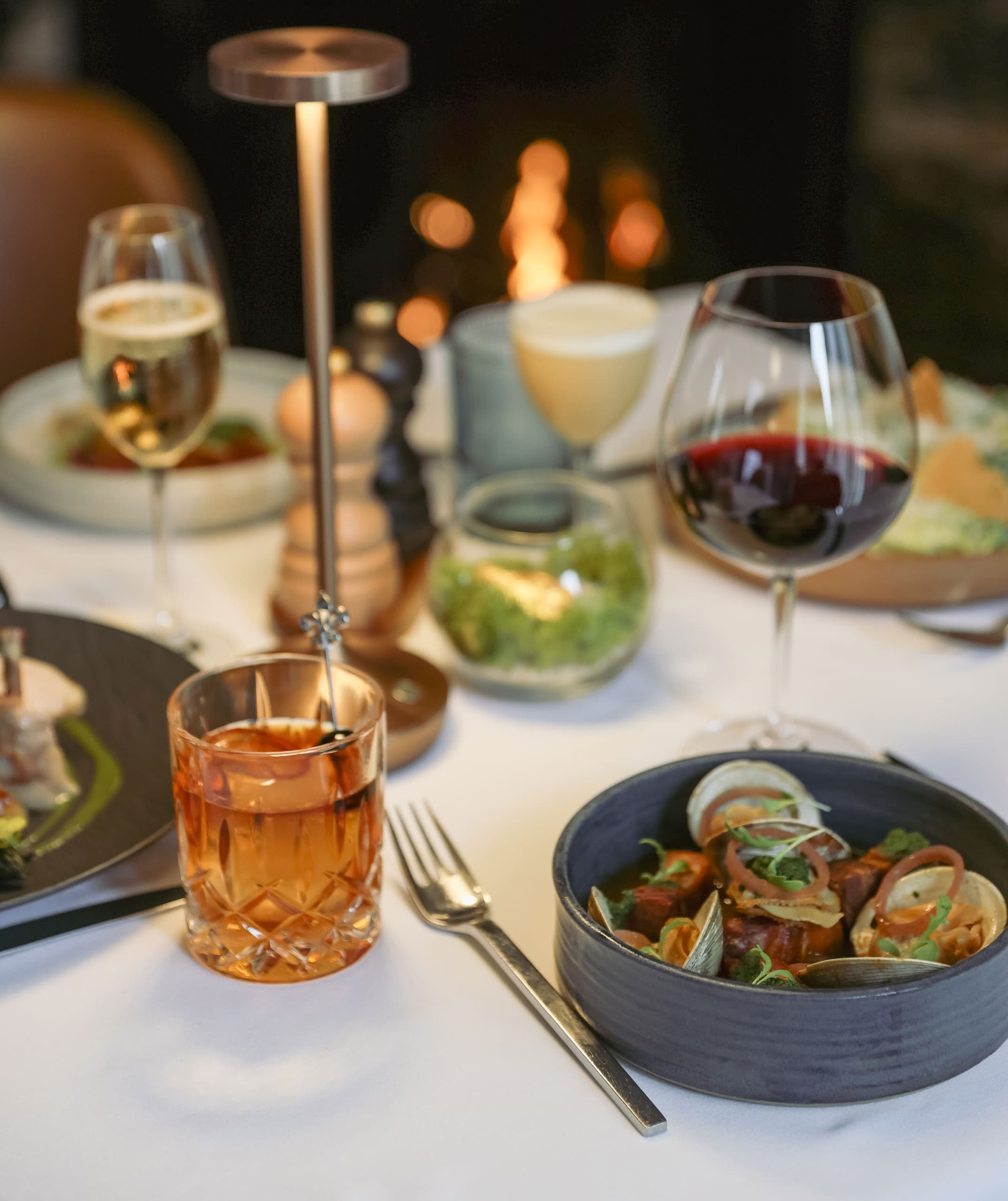 Seasonal seafood entrée with a craft cocktail and red wine by the fire at Chatham Inn's restaurant in Chatham, Massachusetts.