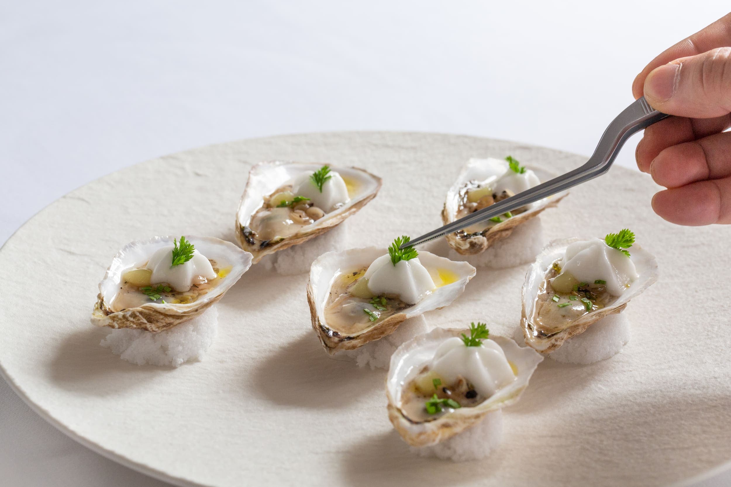 A chef placing herbs on oysters with tweezers at Cuvee restaurant at Chatham Inn