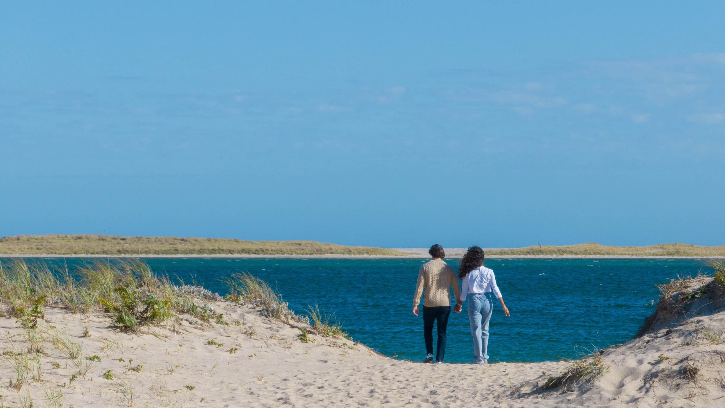 A couple holding hands walking towards the water on the beach