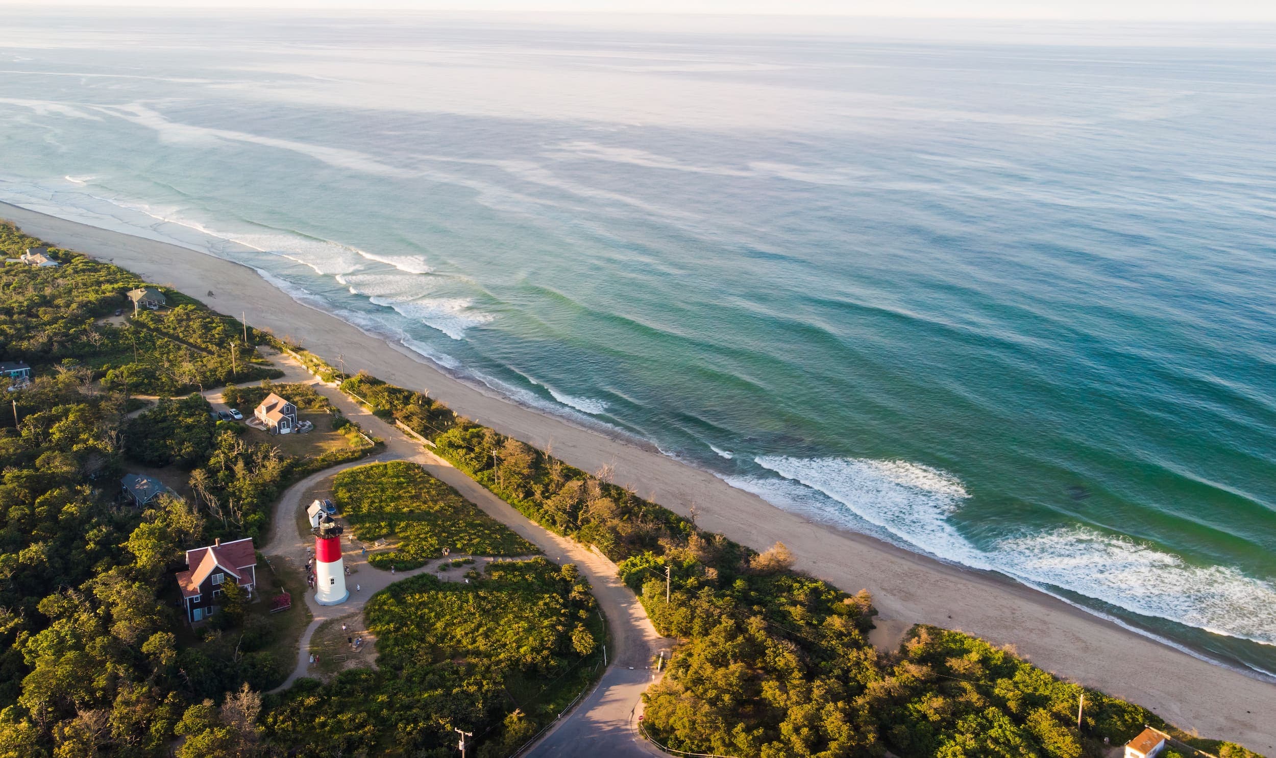 An aerial view of the ocean and the beach with a lighthouse just off the beach