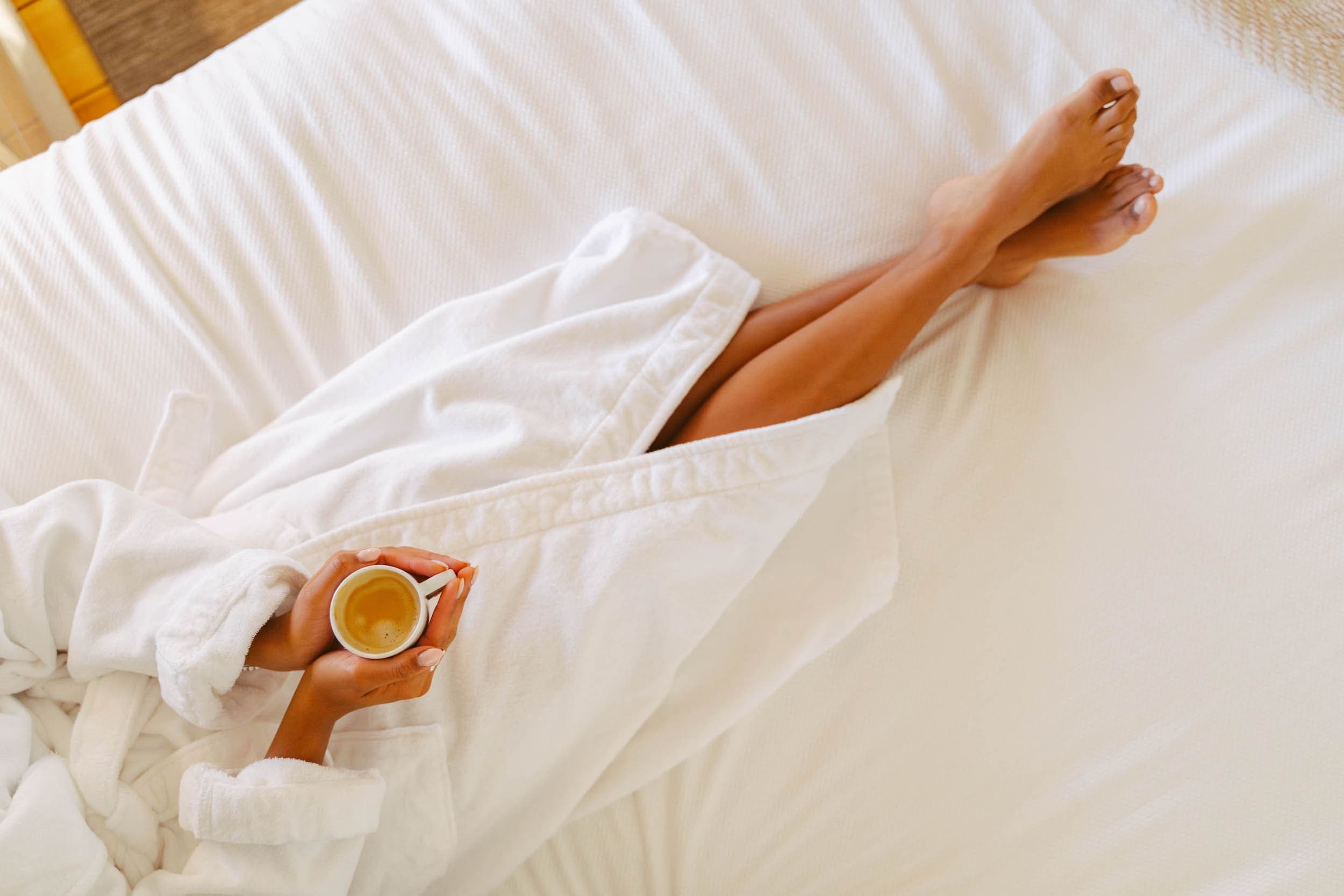 A woman laying in bed with a coffee in her hands in a room at Chatham Inn