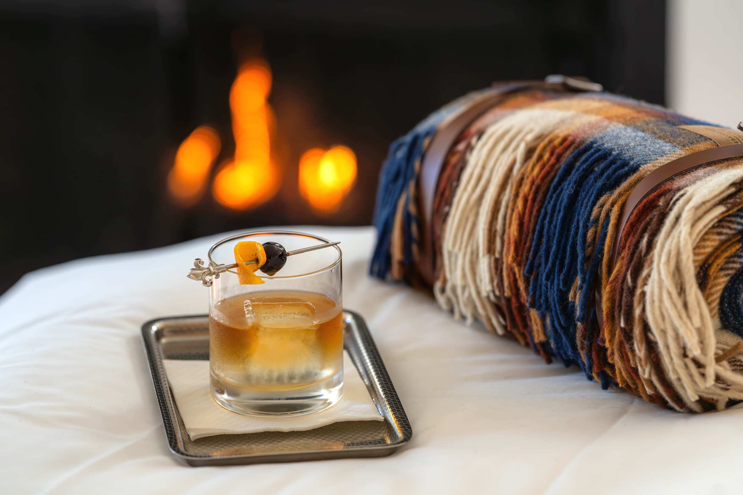 A cocktail on a bed in a room at Chatham Inn with a rolled blanket and a fireplace