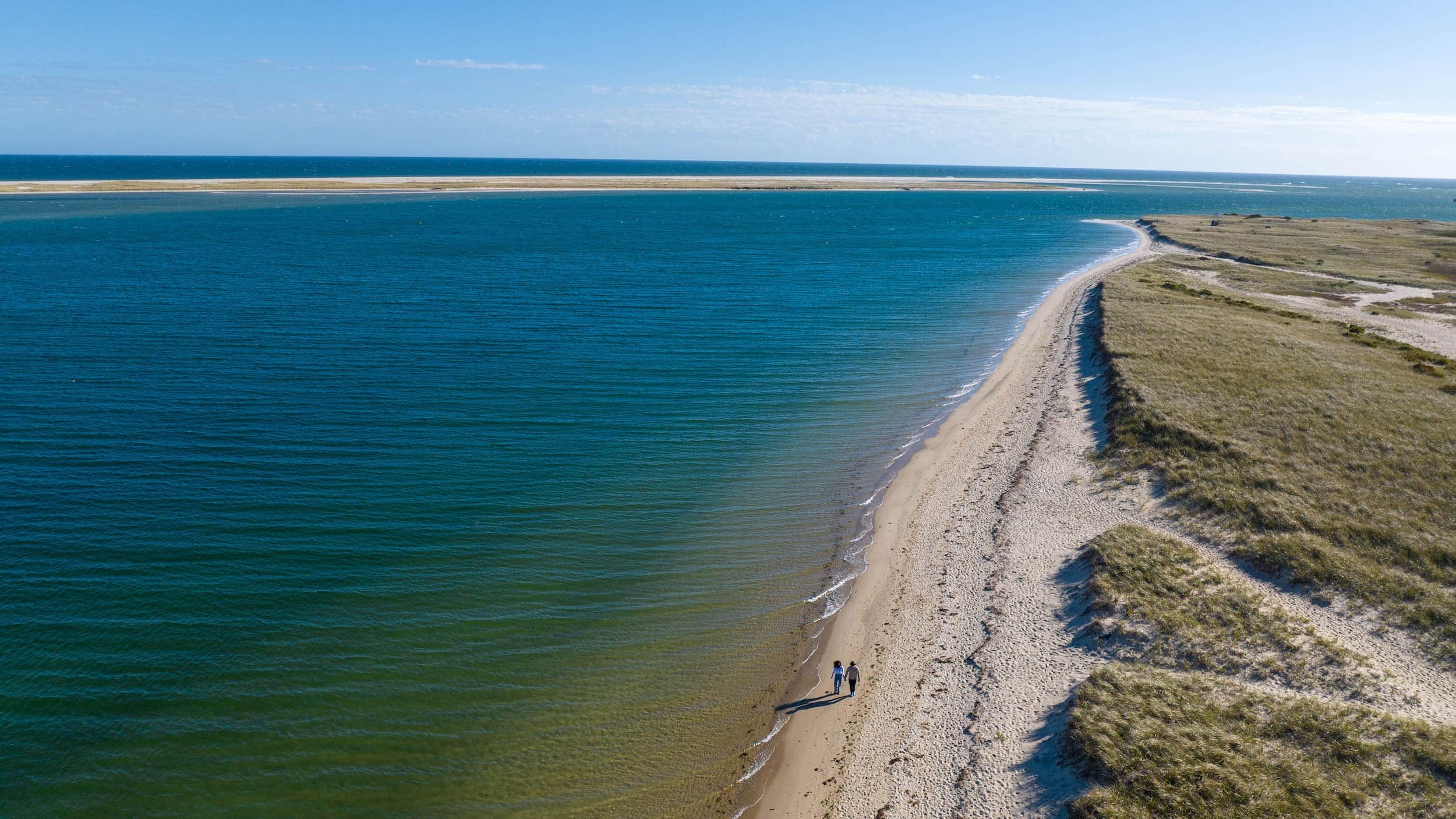 A couple holding hands walking the shoreline of open water near Chatham Inn