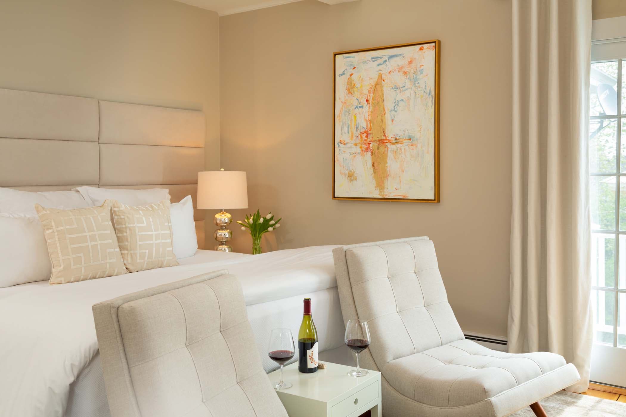 A king bed with two chairs at the end of the bed in Room 11 at Chatham Inn