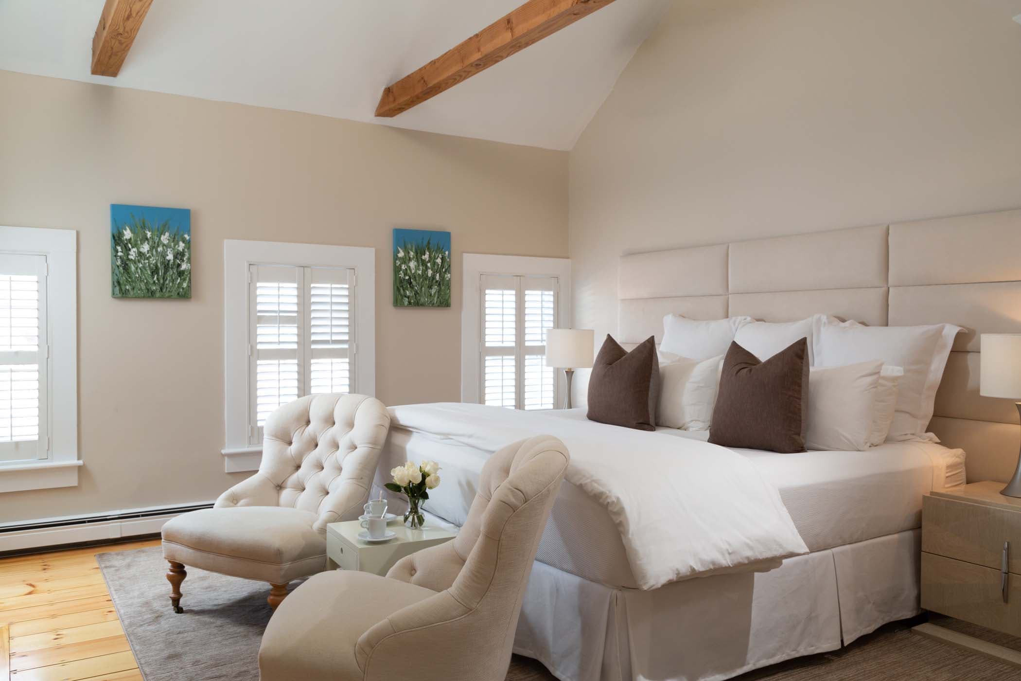 A king bed, 3 large windows, and two chairs in Room 17 at Chatham Inn