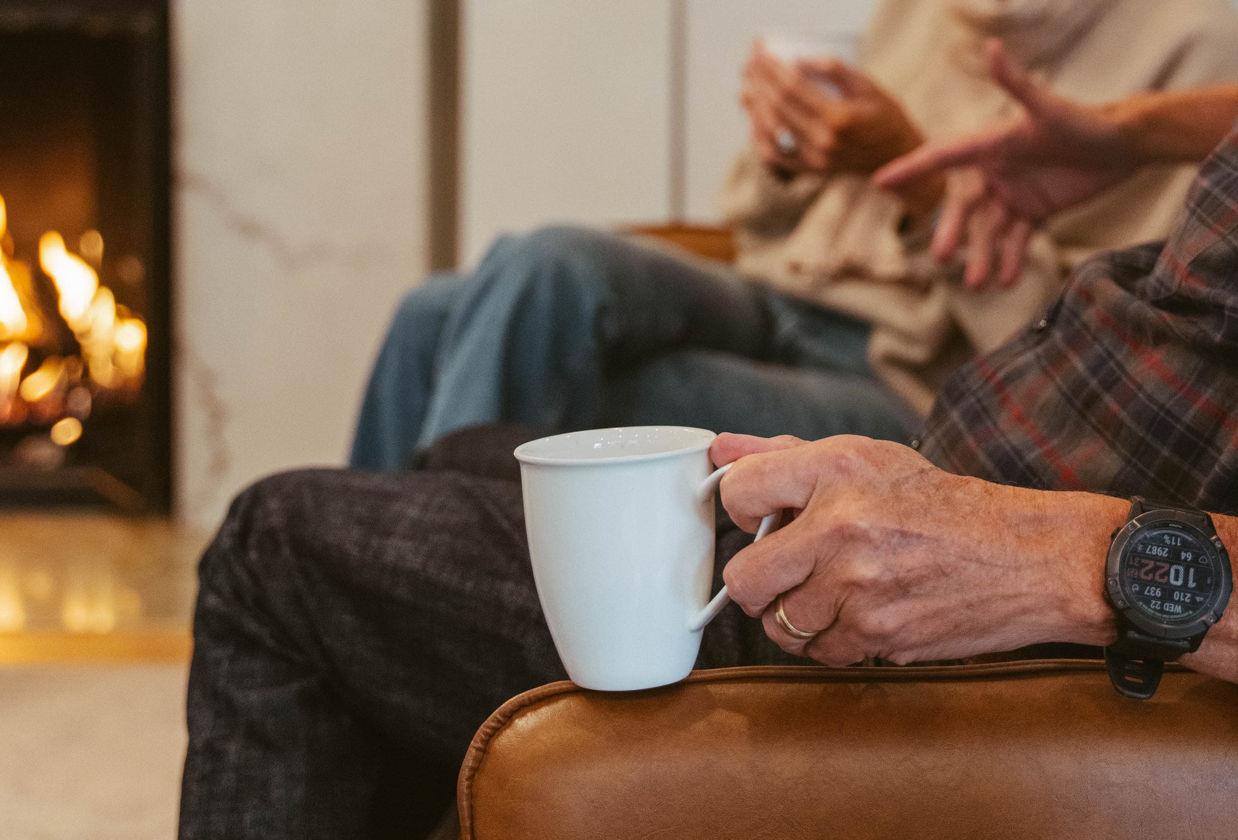A man and a woman enjoying a hot beverage in their room with a fireplace at the Chatham Inn